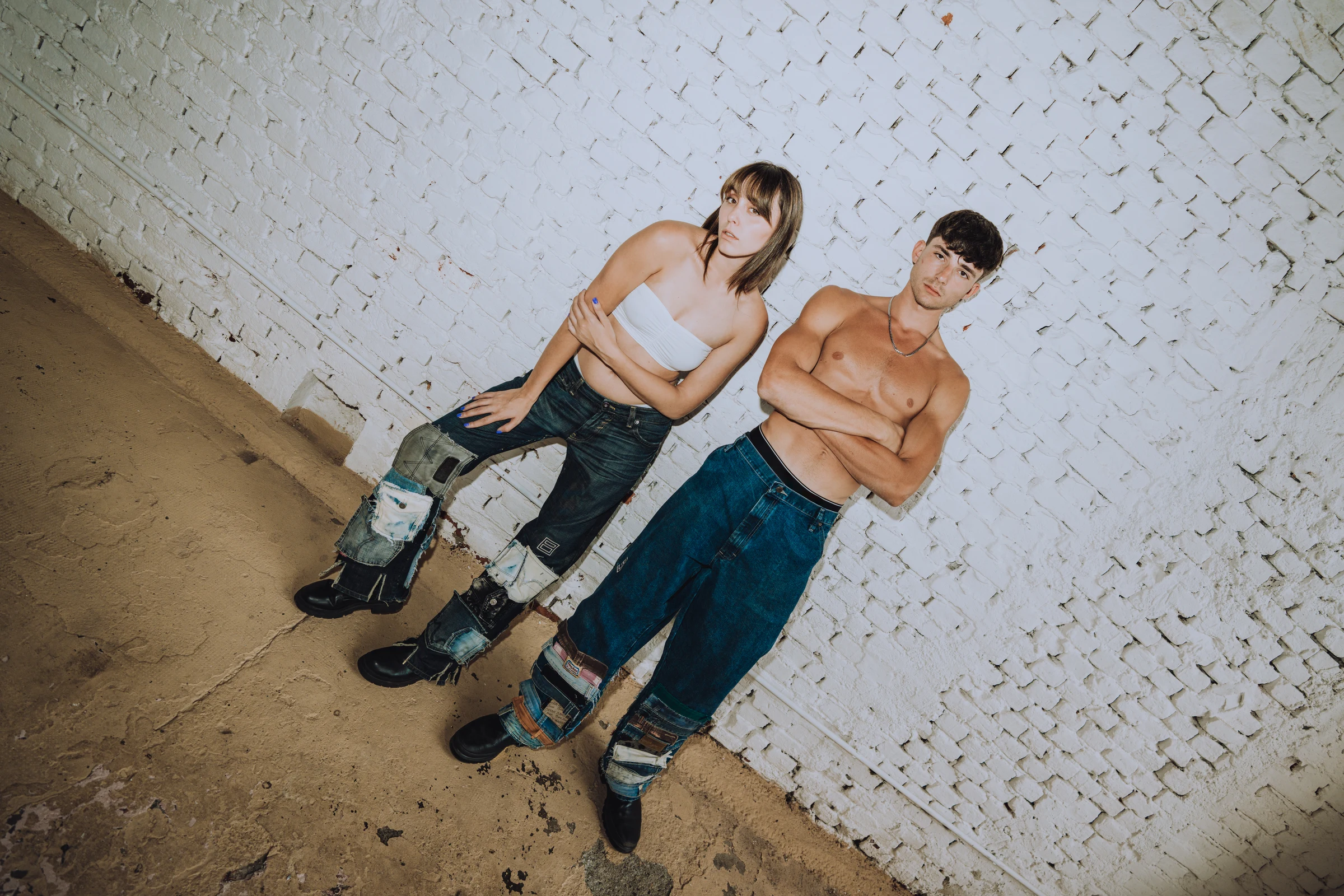Two fashion models in jeans against a white brick wall
