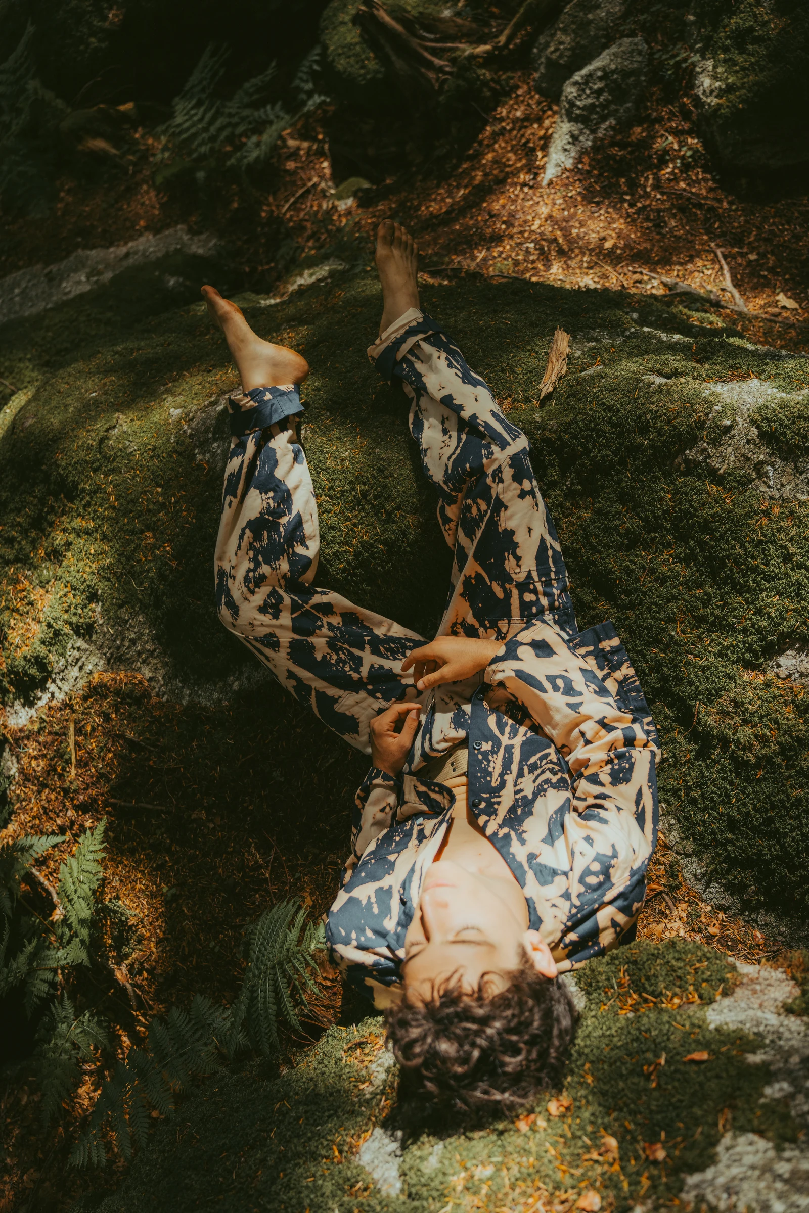 Model in patterned clothing lying on a forest floor