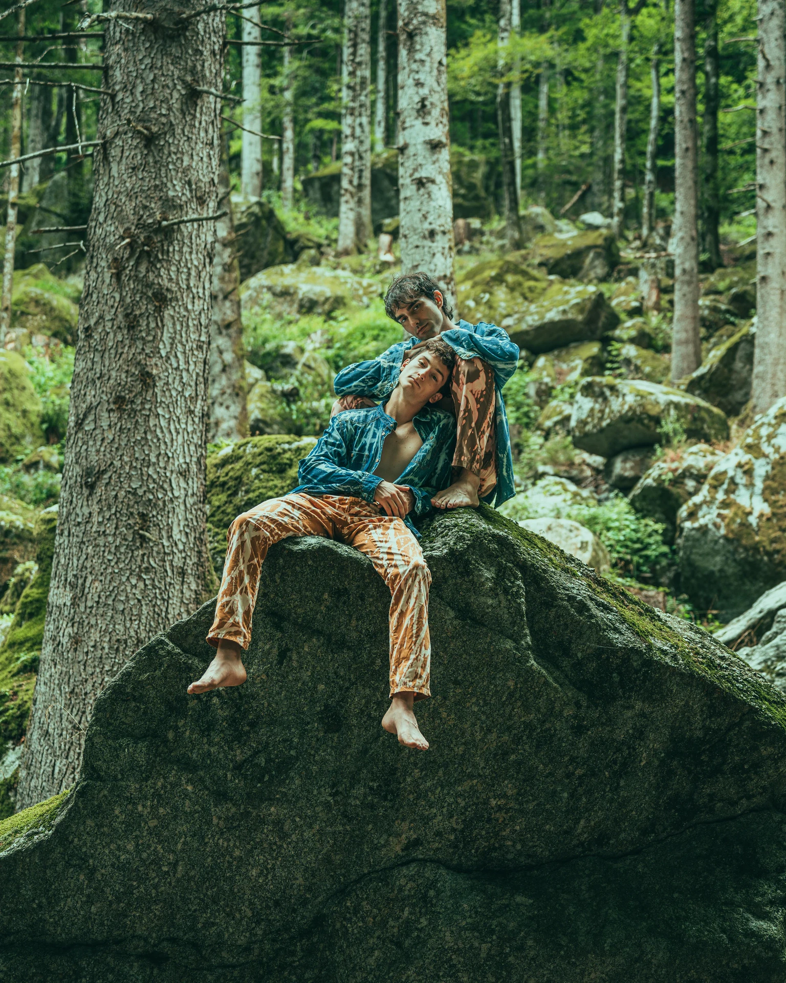 Model in a patterned suit seated on a rock in a forest