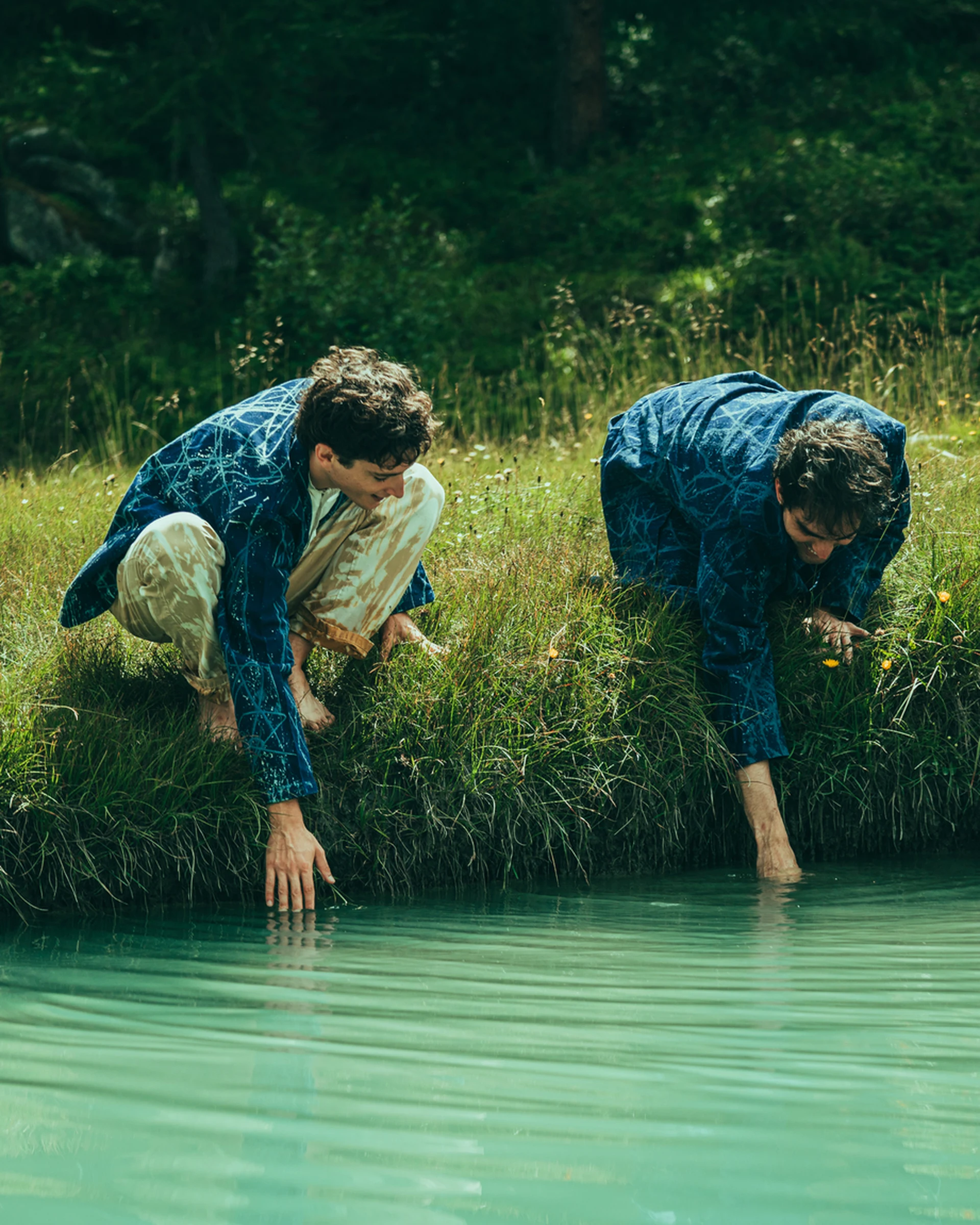 Two models beside turquoise water in a natural landscape