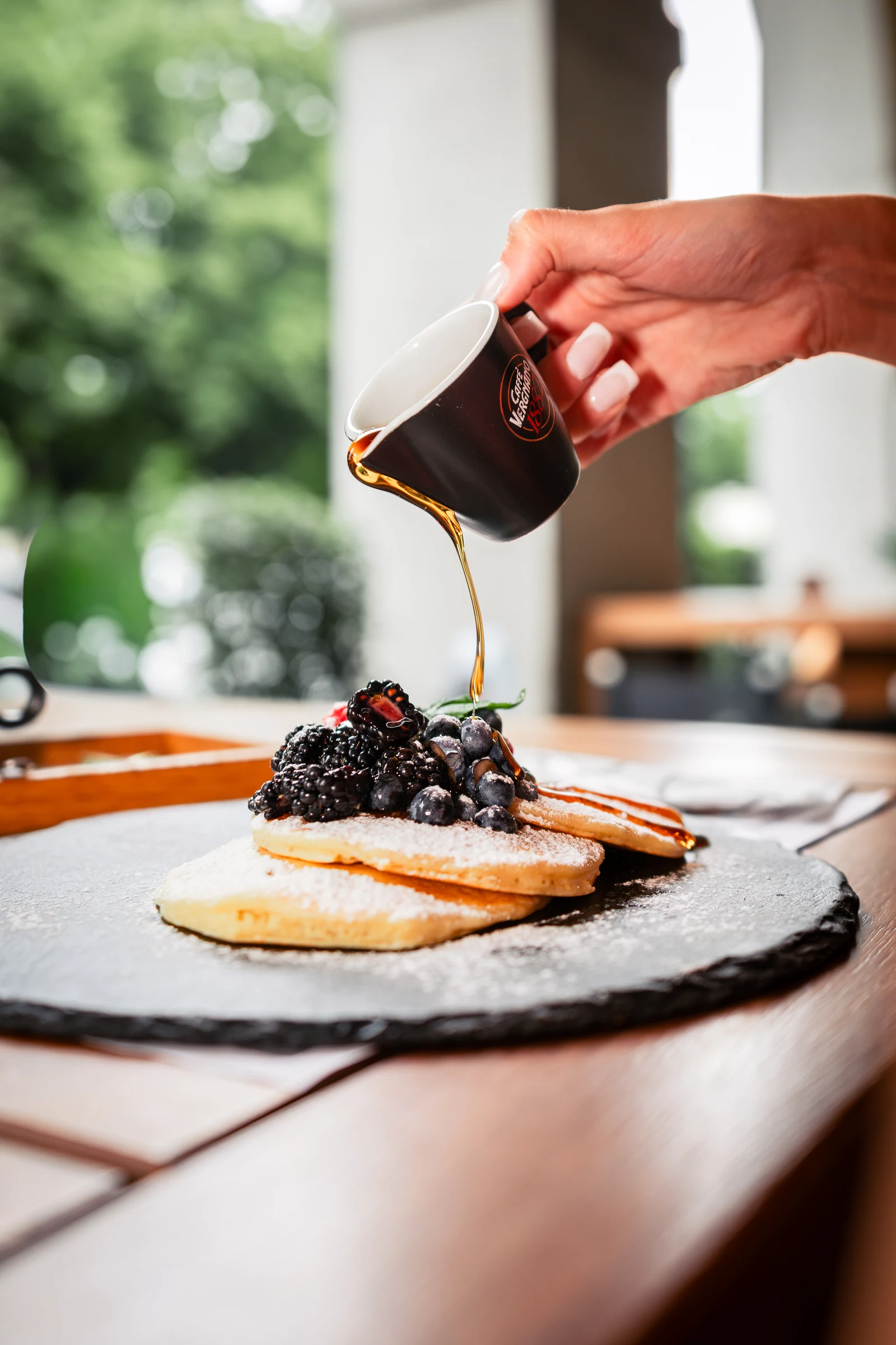 Syrup being poured over berry-topped pancakes
