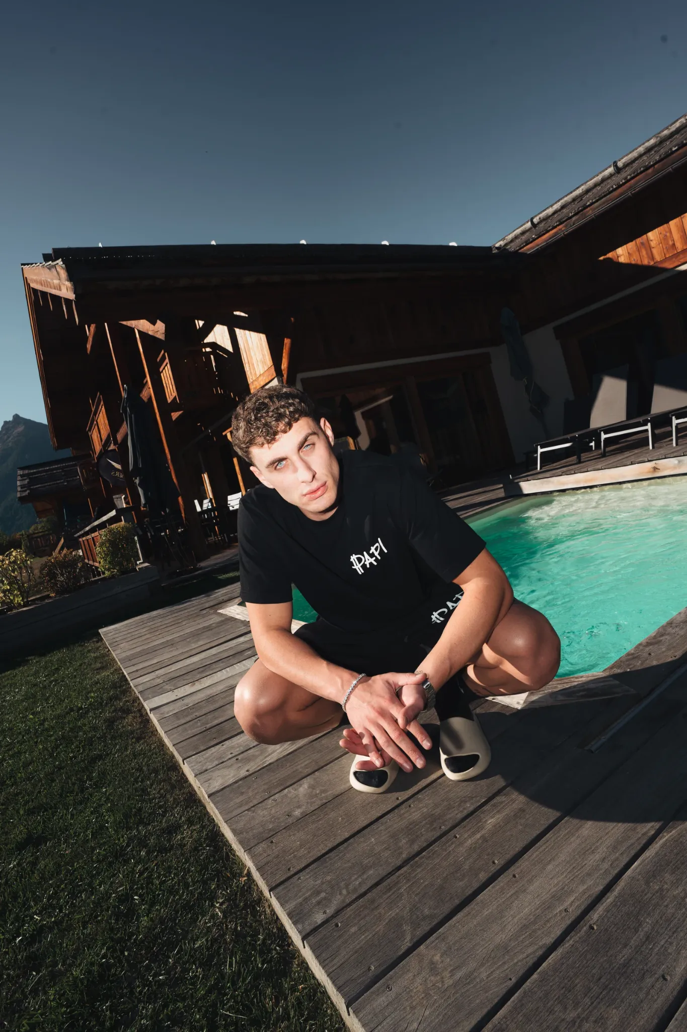 Male lifestyle portrait beside an outdoor swimming pool and alpine chalets