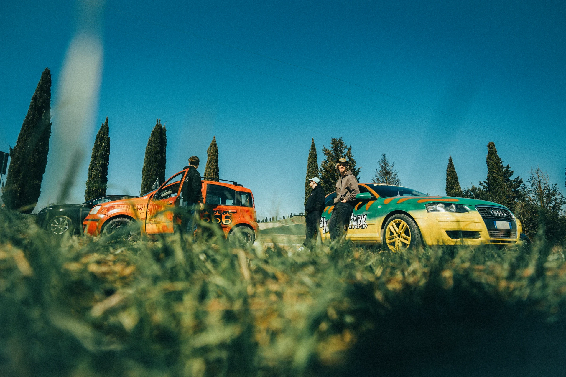 Three people standing beside rally cars on an outdoor track